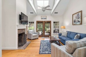A living room with a fireplace, a blue sofa, a television mounted on the wall, and a ceiling fan.