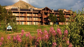 A multi-story lodge with balconies, a mountain backdrop, and a sign indicating a ski resort. - Home Away From Home! Ski-in/Ski-out, Dog Friendly Condo w/ Fireplace & Views (Mt. Crested Butte)
