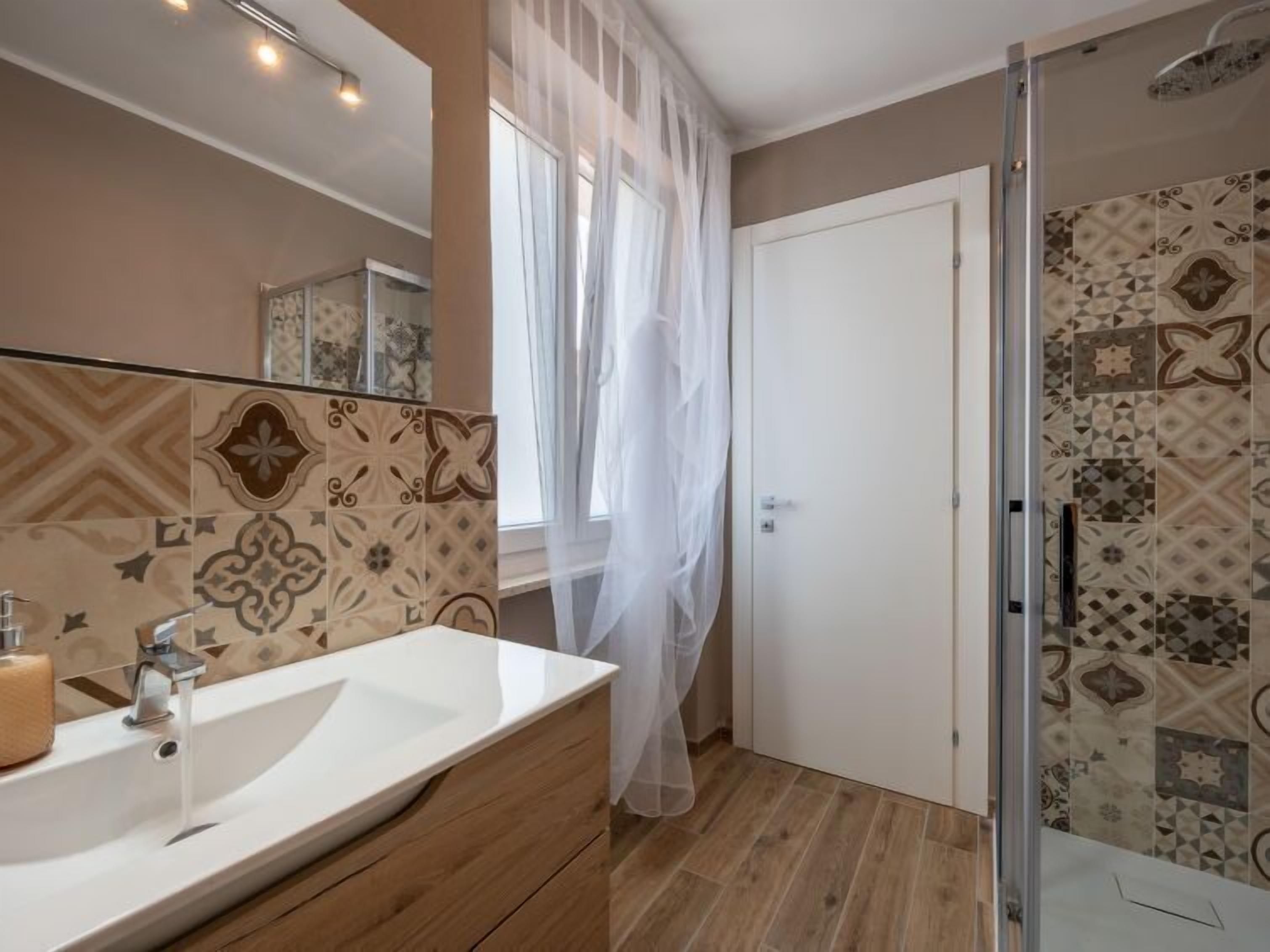 A bathroom with a white sink, a glass shower enclosure, and patterned tiles.