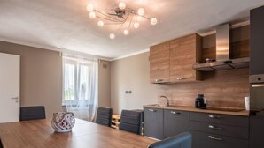 Een moderne keuken met donkere kasten, een houten aanrecht en een kroonluchter. Er staat een eettafel met stoelen en een vaas op.