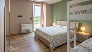 Een slaapkamer met een stapelbed, een enkel bed, een raam met gordijnen, een plafondlamp en een radiator.