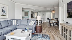 A modern living room with a grey sectional sofa, a white coffee table, and a dining area with a wooden table and chairs.