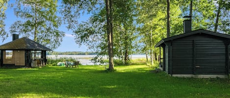 A grassy area with a small wooden cabin and a gazebo near a body of water.