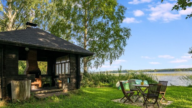 Un chalet rustique doté d’une cheminée en briques, d’une petite terrasse et d’une table avec des chaises, le tout offrant une vue sur un lac.