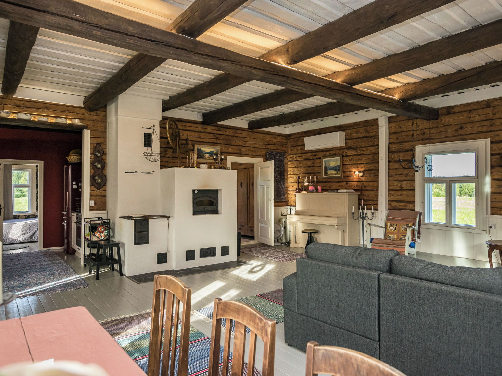 A cozy living room with a fireplace, wooden beams, and a large window.