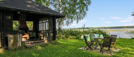 A rustic cabin with a chimney, a small porch, and a table with chairs outside.