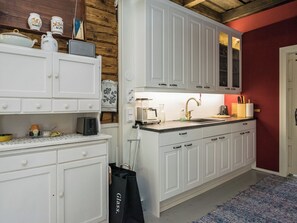 Una cocina con armarios blancos, una encimera con varios electrodomésticos y una pared roja.