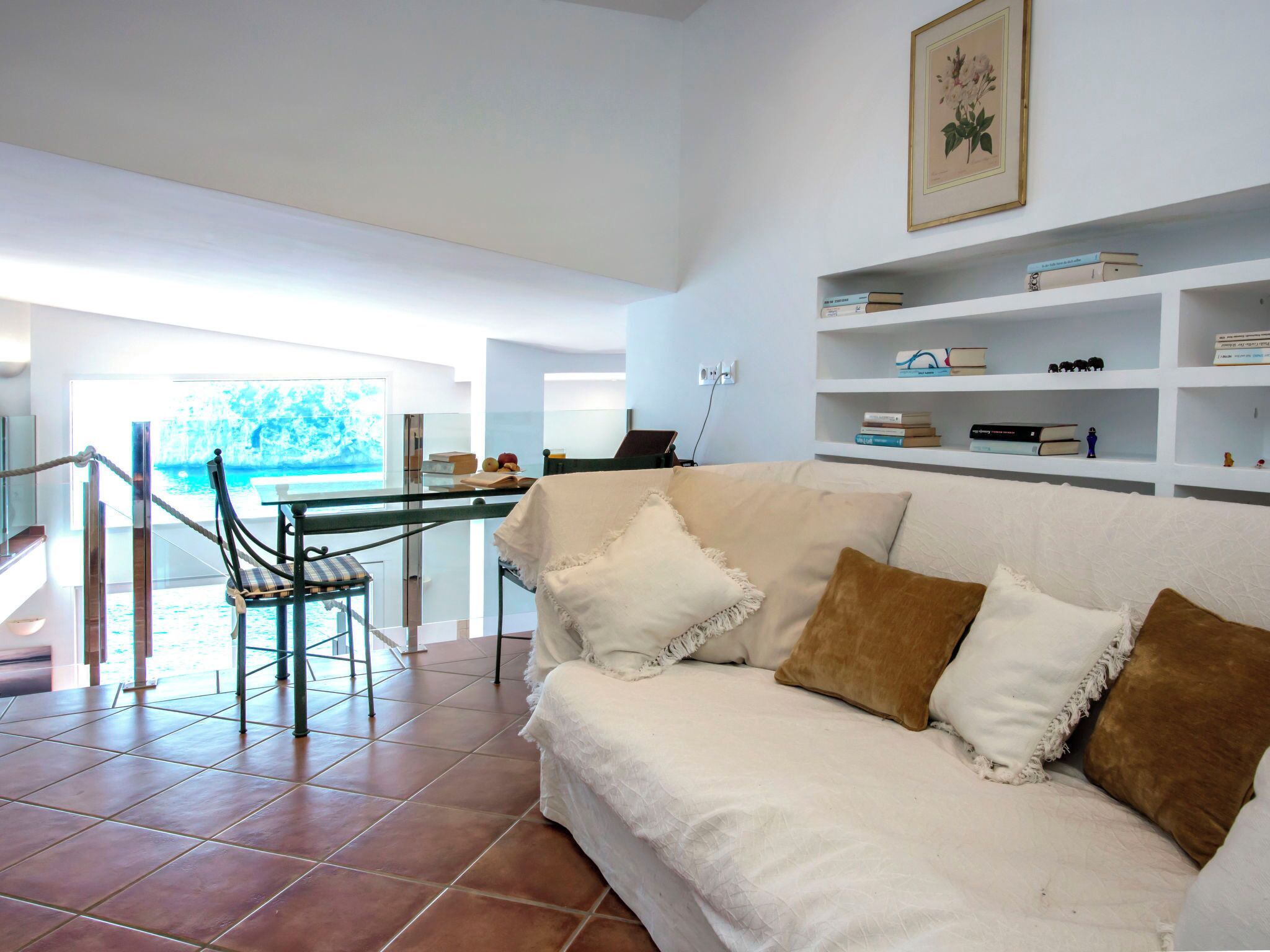 A spacious living area with a white sofa, a glass table, and a view of the sea.