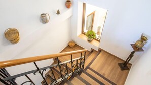 Uma escada de madeira com corrimão de metal, uma pequena janela com uma planta e objetos decorativos na parede.