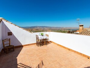 Una terraza en la azotea con mesa y sillas, vistas al campo y un cielo azul despejado.
