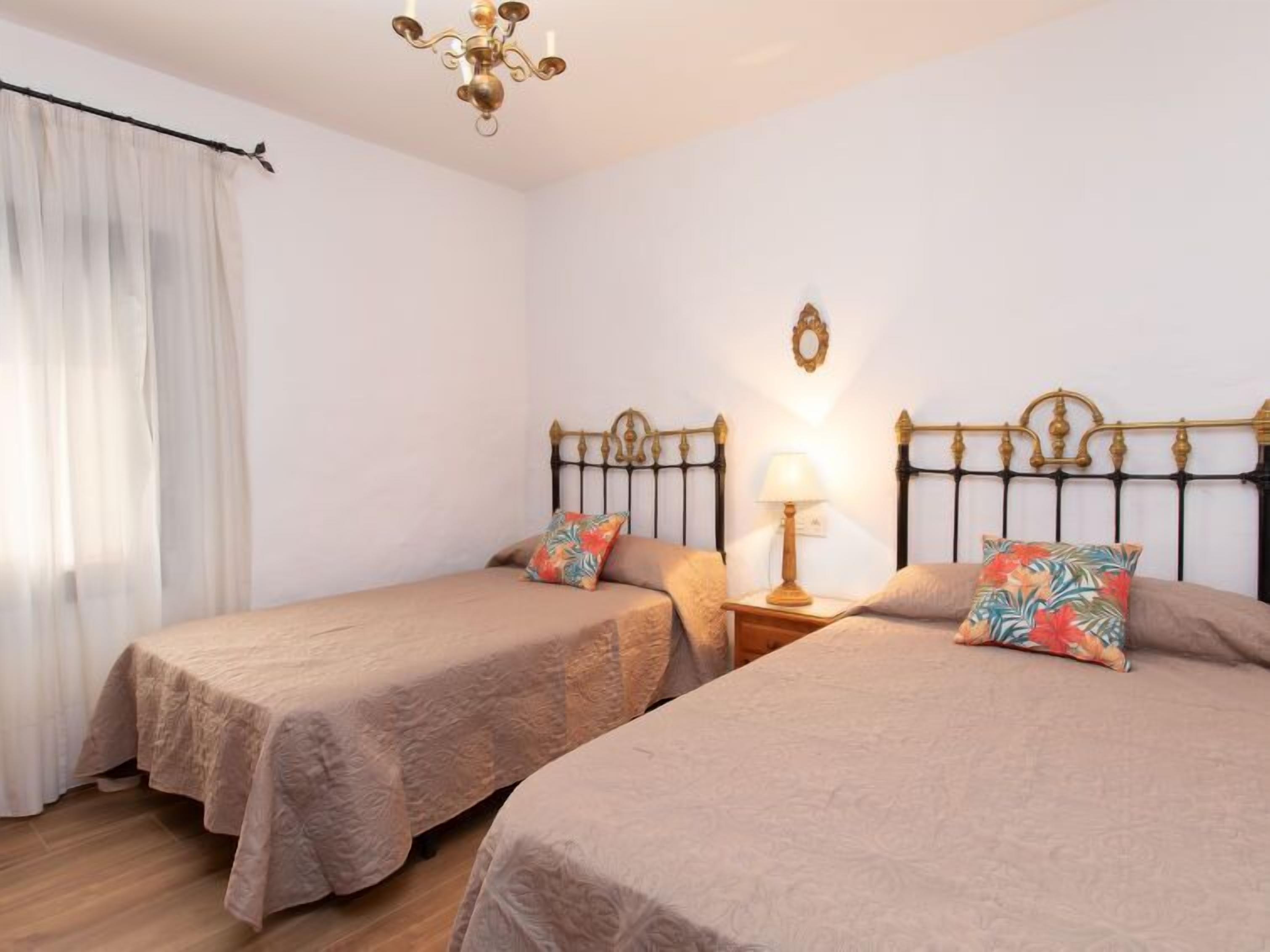 Ein Zimmer mit zwei Betten, einer Deckenleuchte, einem Nachttisch mit Lampe und einem fenster mit Vorhängen.
