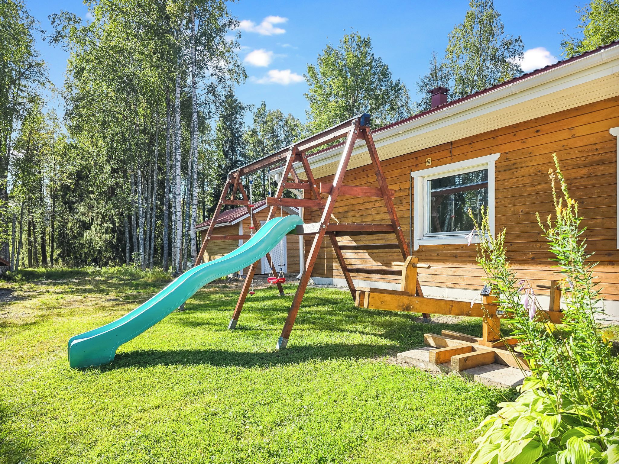 En stuga av trä med en rutschkana och en klätterställning, belägen i ett skogsområde.