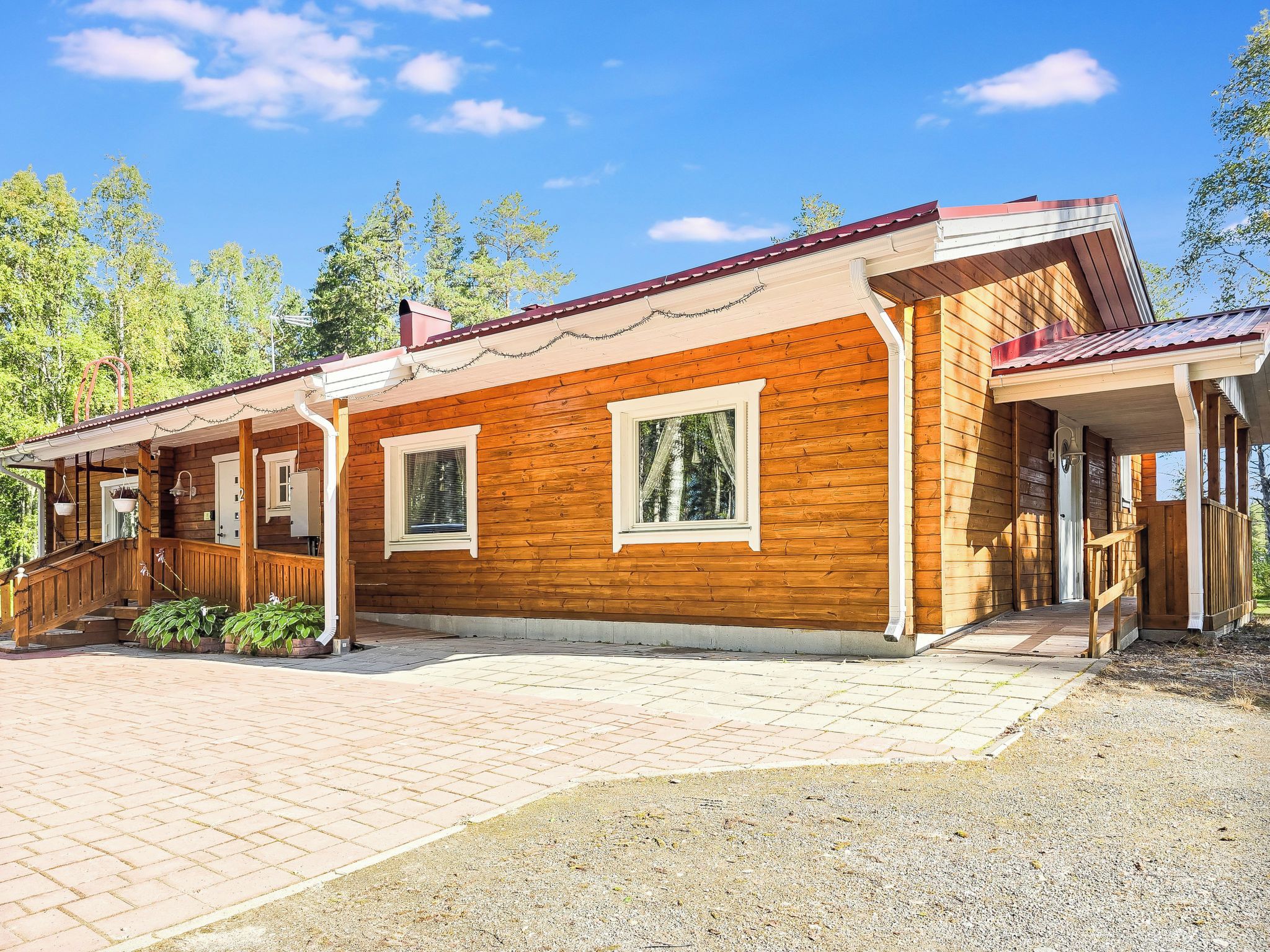 A wooden cabin with a covered porch, a staircase, and a gravel driveway.