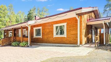 A wooden cabin with a covered porch, a staircase, and a gravel driveway.