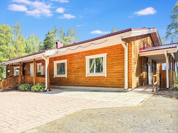 A wooden cabin with a covered porch, a staircase, and a gravel driveway.
