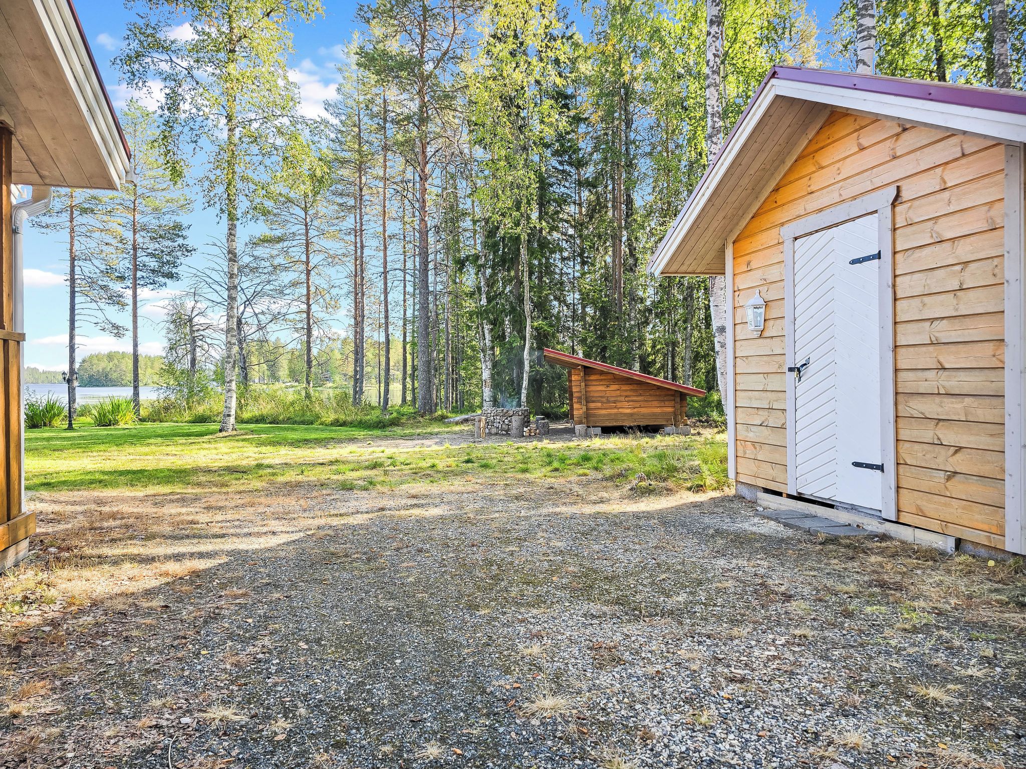 A wooden cabin with a gravel driveway, surrounded by a forest.