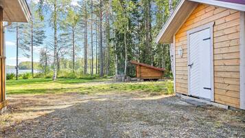 A wooden cabin with a gravel driveway, surrounded by a forest.