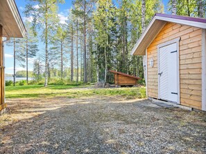A wooden cabin with a gravel driveway, surrounded by a forest.
