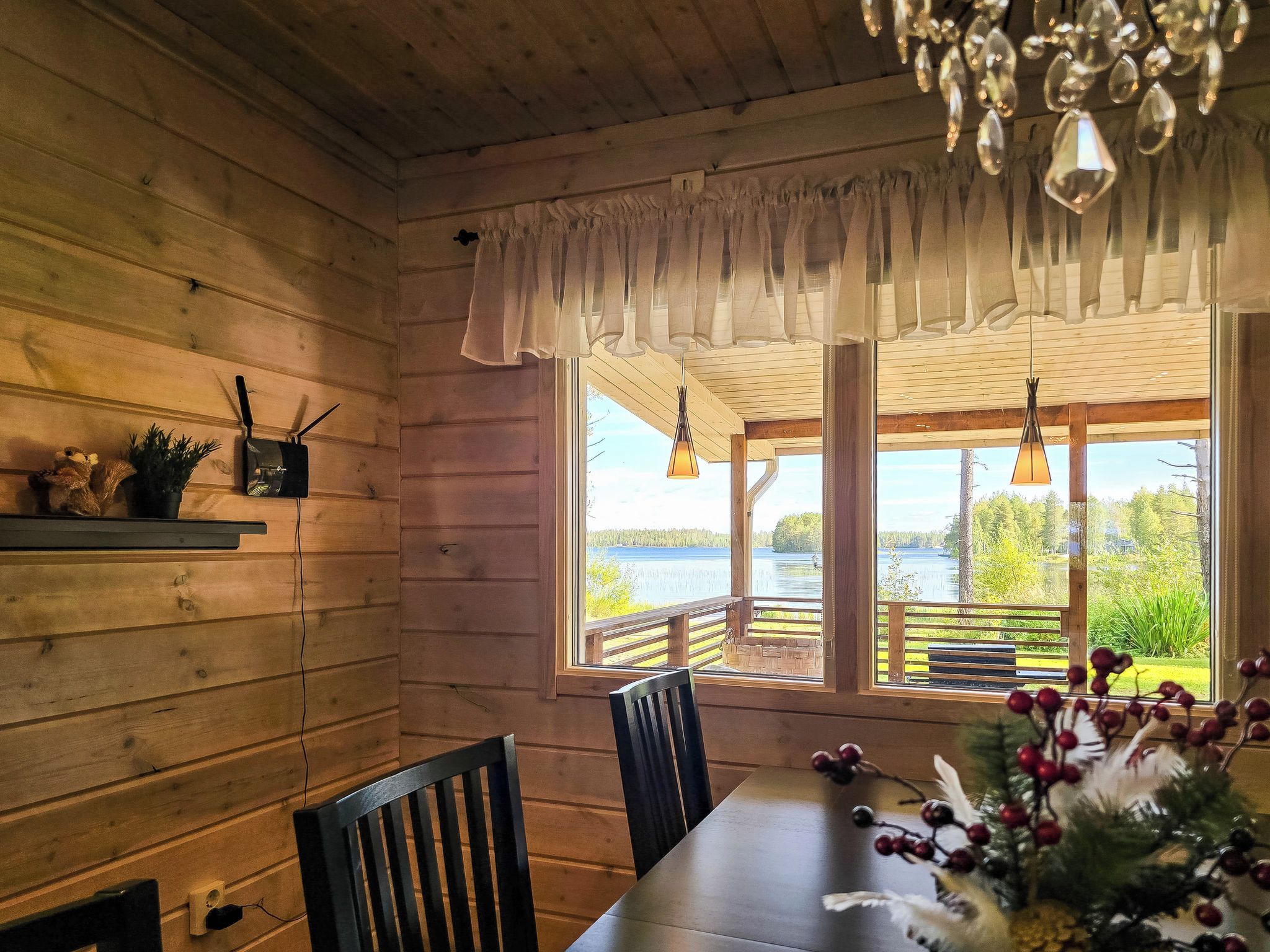 L’intérieur d’un chalet en bois, avec une table à manger, des chaises, un lustre et une vue sur un lac.