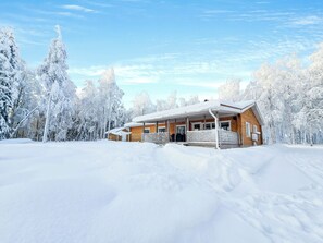 A wooden cabin with a porch, surrounded by snow-covered trees.