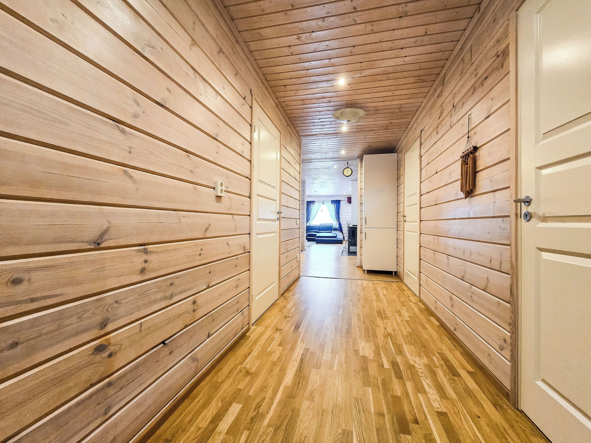 A hallway with wooden walls and a wooden floor leading to a room with a bed and a window.