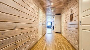 A hallway with wooden walls and a wooden floor leading to a room with a bed and a window.