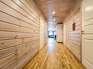 A hallway with wooden walls and a wooden floor leading to a room with a bed and a window.
