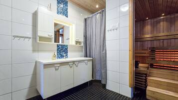 A bathroom with a white vanity, a mirror, a blue mosaic tile, a shower curtain, and a wooden sauna door.