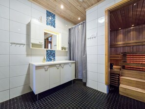 A bathroom with a white vanity, a mirror, a blue mosaic tile, a shower curtain, and a wooden sauna door.