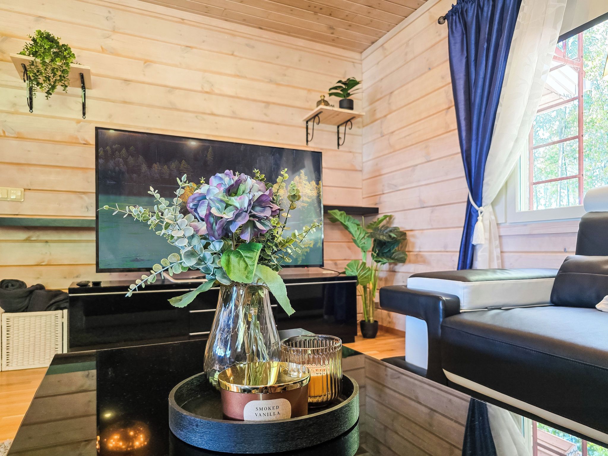 Una sala de estar moderna con un televisor de pantalla plana, un sofá, una mesa de centro con un jarrón de flores y una bandeja con velas.