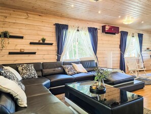 A modern living room with a sectional sofa, a glass coffee table, and a view of the outdoors through large windows with curtains. - Oravajärven talo (ent. suomela) by Interhome (Ranua)