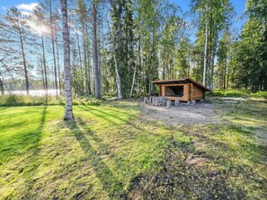 A wooden cabin with a stone foundation, surrounded by a forest and a lake.