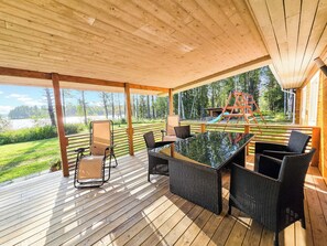 A covered outdoor area with a wooden deck, wicker furniture, and a view of a playground.