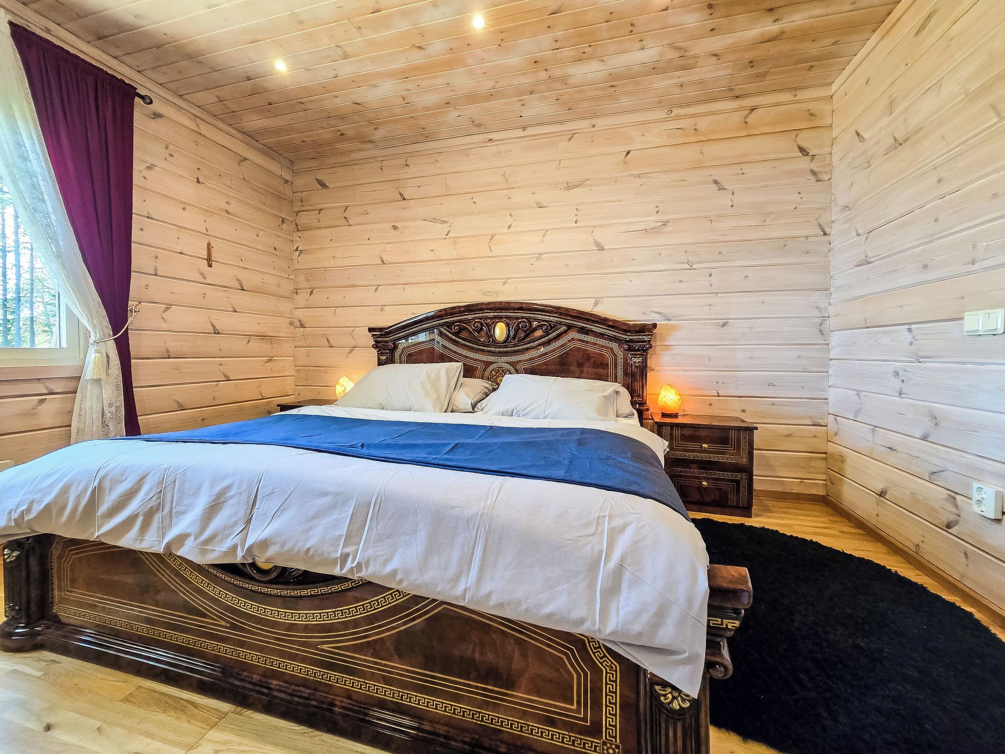 Una habitación con paneles de madera, una cama, una mesita de noche y un ventanal con cortinas.