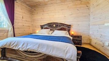 Una habitación con paneles de madera, una cama, una mesita de noche y un ventanal con cortinas.