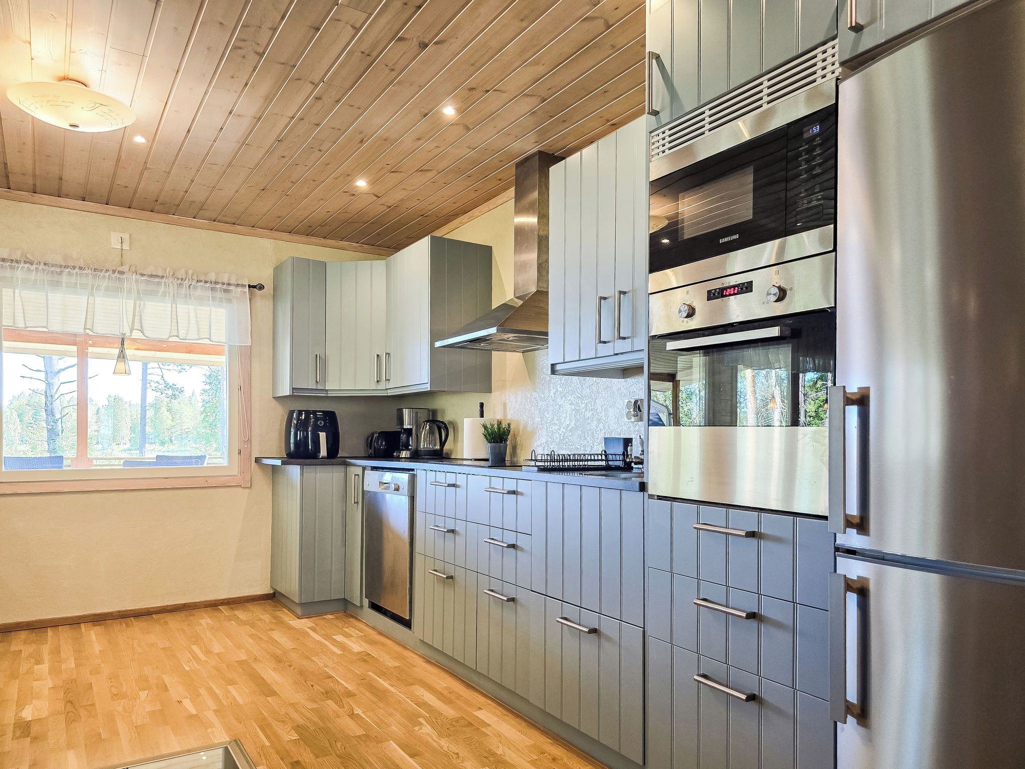 A modern kitchen with grey cabinets, stainless steel appliances, and a wooden ceiling.
