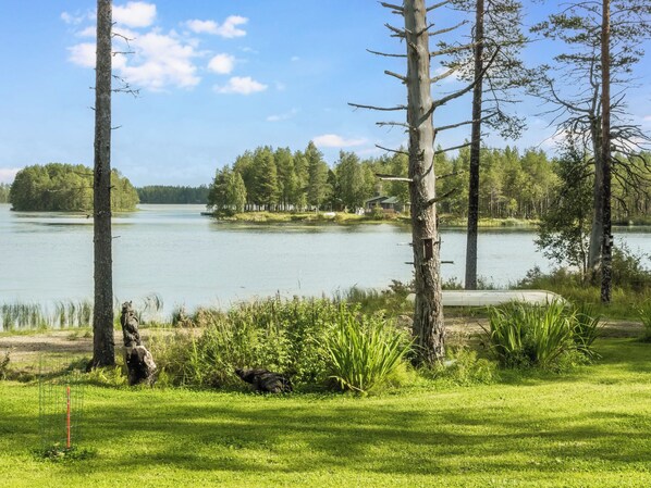 A lakeside property with a grassy area, trees, and a small cabin.