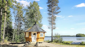 A small wooden cabin with a chimney, surrounded by trees and a lake.