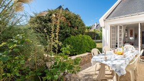 A patio with a table set for dining, surrounded by greenery and a stone wall. - Kergroix by Interhome (Quiberon)
