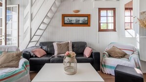 A cozy living room with a black leather sofa, a white coffee table, and a striped armchair. A ladder is visible against the wall, and a framed picture hangs above the sofa. - Kergroix by Interhome (Quiberon)