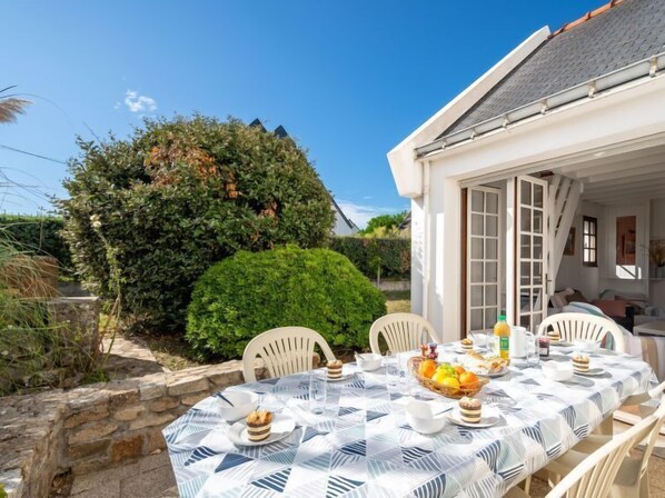 An outdoor dining area with a table set for four, surrounded by white chairs, under a clear sky.