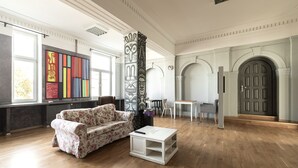 Ein geräumiges Wohnzimmer mit einem blumengedeckten Sofa, einem weißen Couchtisch und einem großen Fenster mit farbenfroher Kunst.