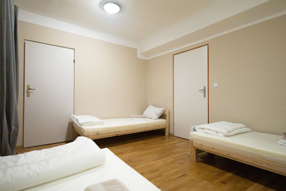 Una habitación con dos camas individuales, suelo de madera y una lámpara en el techo.