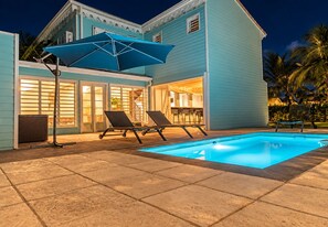 Una casa con piscina, dos sillones de descanso y una sombrilla.