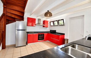 Una cocina moderna con armarios rojos, electrodomésticos de acero inoxidable y encimera negra.