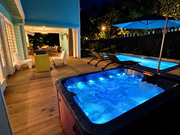 Un jacuzzi con terraza de madera, asientos exteriores y una piscina.