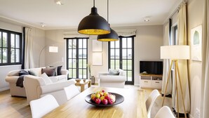 A modern living room with a wooden dining table, white sofas, and a large window with curtains. - Reetdachhaus in Dranske (Dranske)