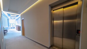Un pasillo con piso alfombrado, un elevador empotrado en la pared y una puerta que da a una habitación con cama y cómoda.