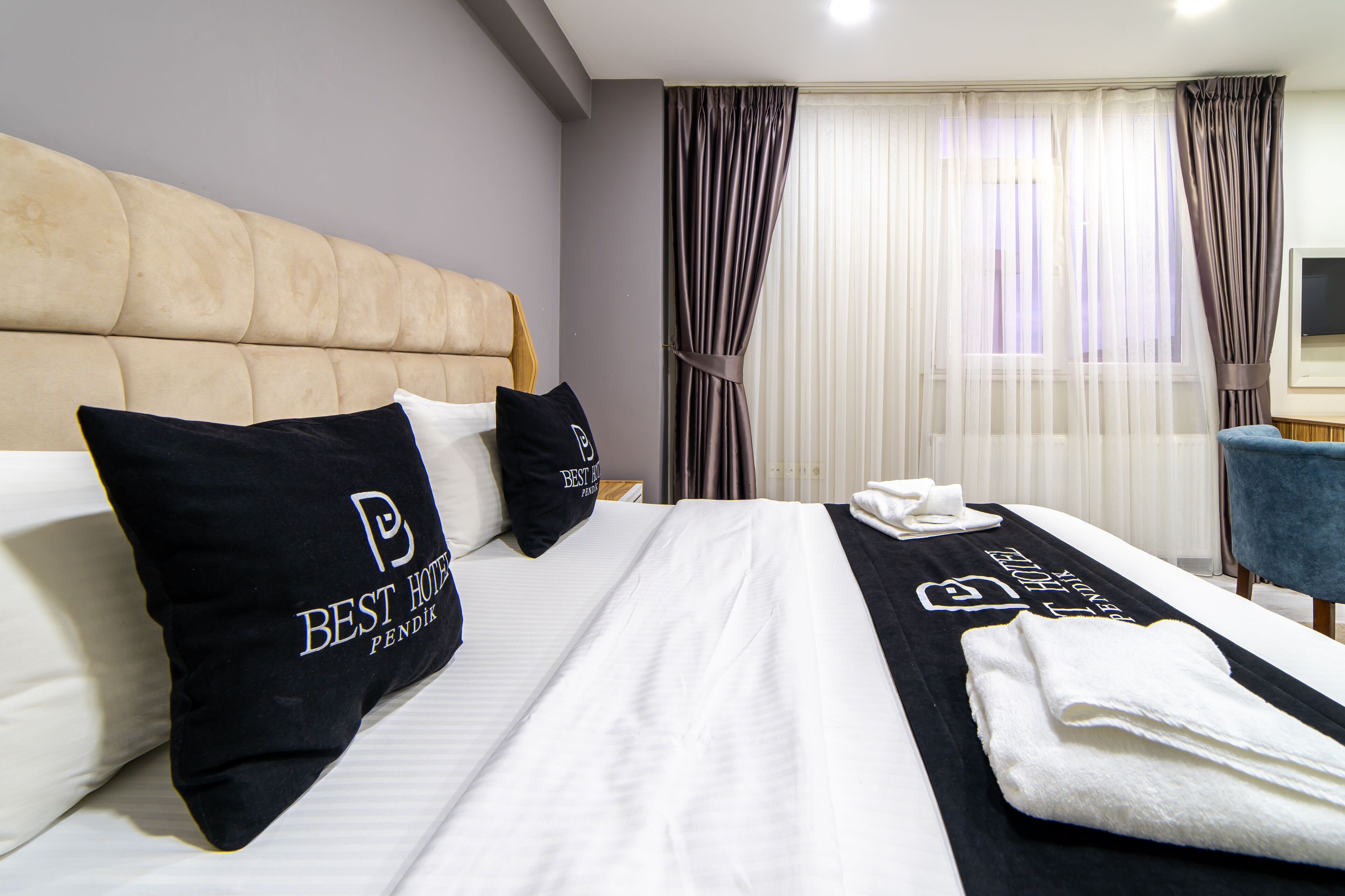 Una habitación de hotel con una cama grande, dos almohadillas negras con el logo del hotel, una colcha blanca y una toalla negra sobre la cama.