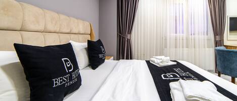 Una habitación de hotel con una cama grande, dos almohadillas negras con el logo del hotel, una colcha blanca y una toalla negra sobre la cama.